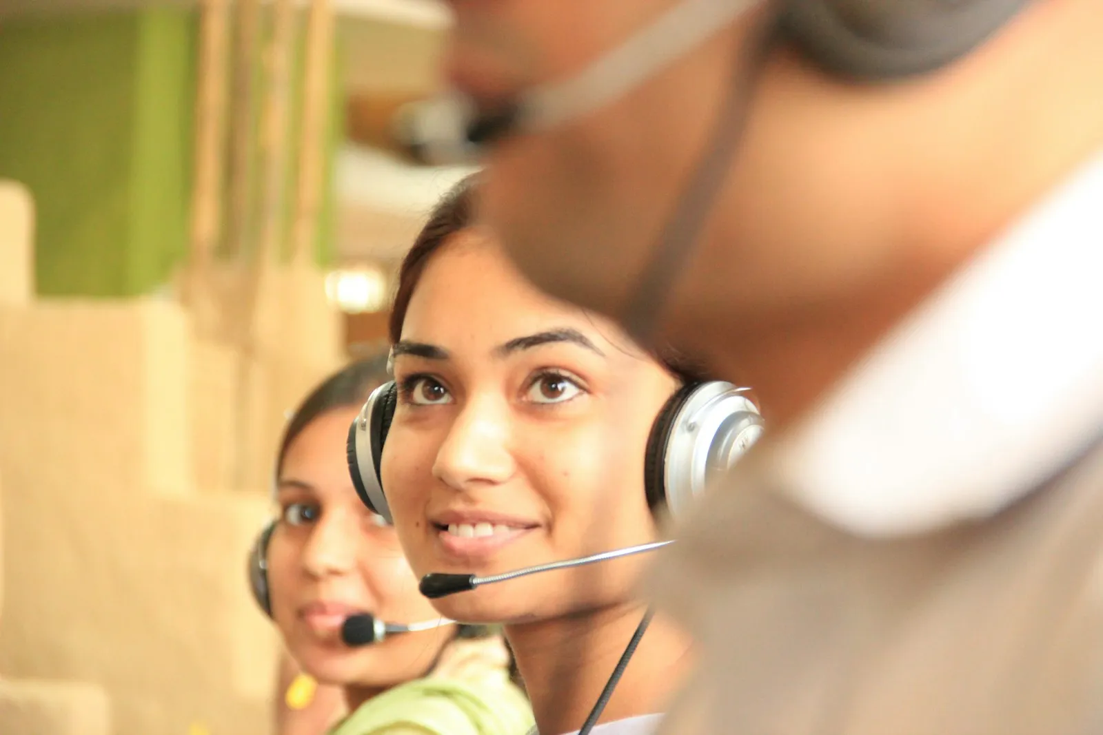 Two women wearing headsets at desks in a bright office workspace