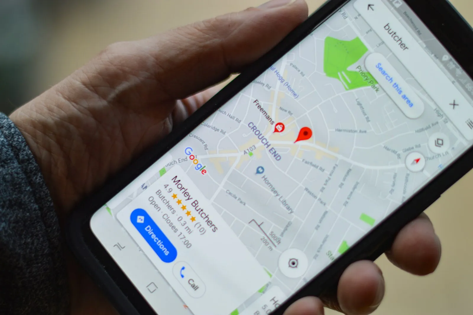 A hand holding a black smartphone that shows a map with a butcher shop listing and a Directions button