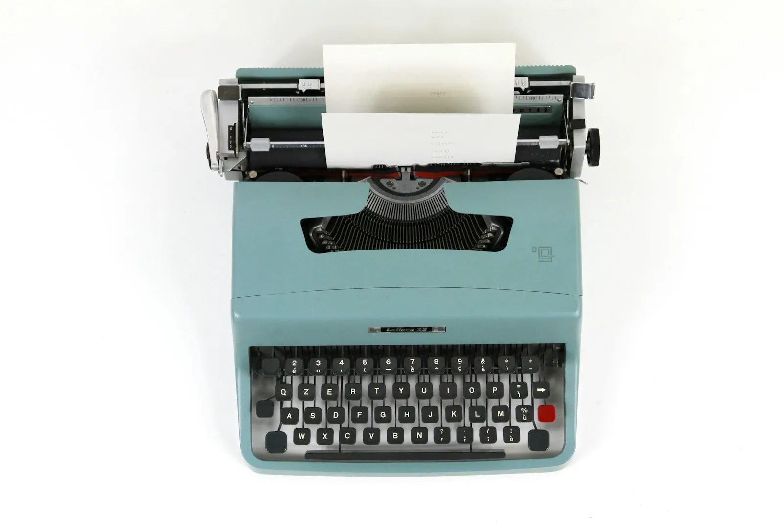 Teal typewriter with a blank sheet of paper on a white background