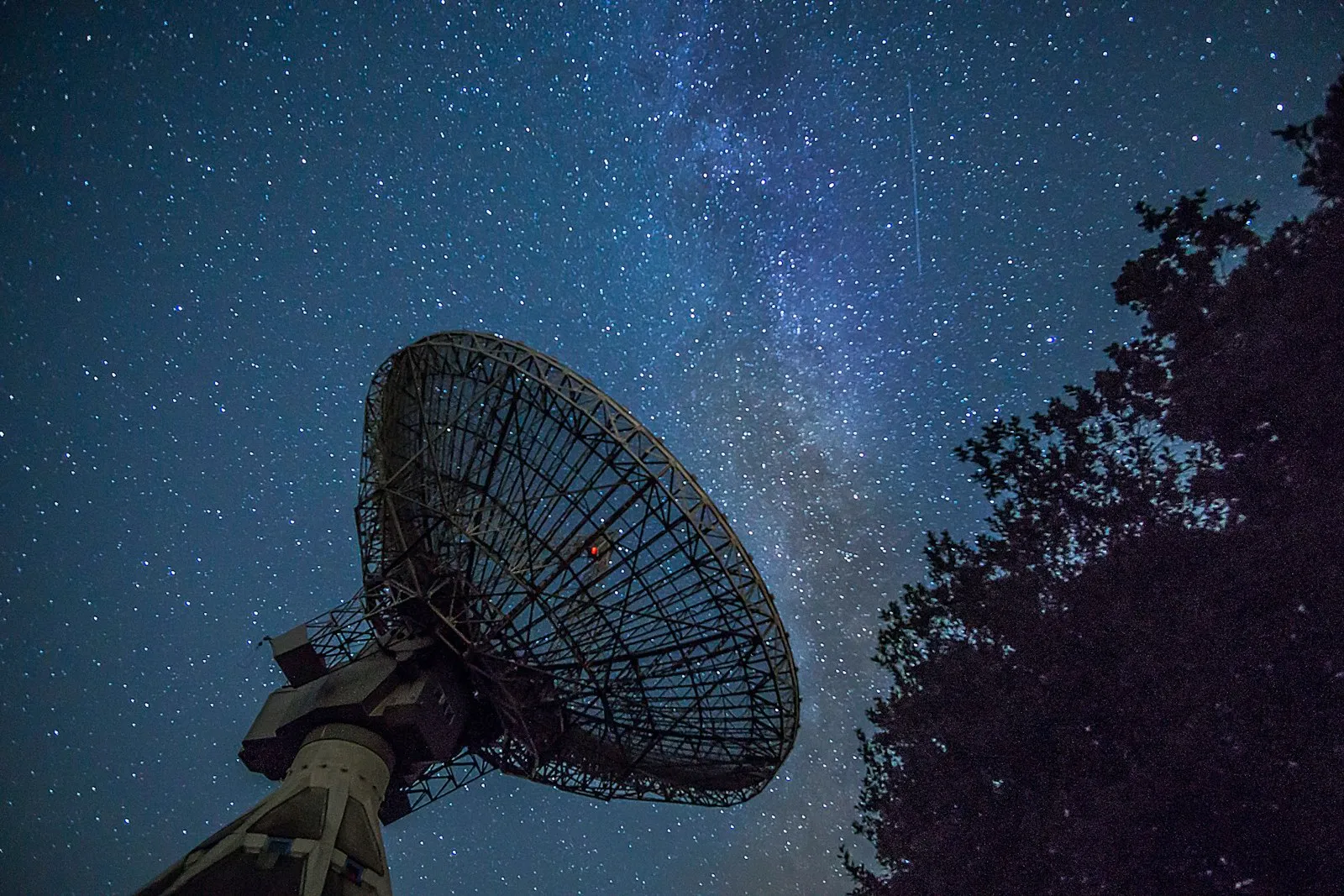 A white satellite dish under a deep blue night sky