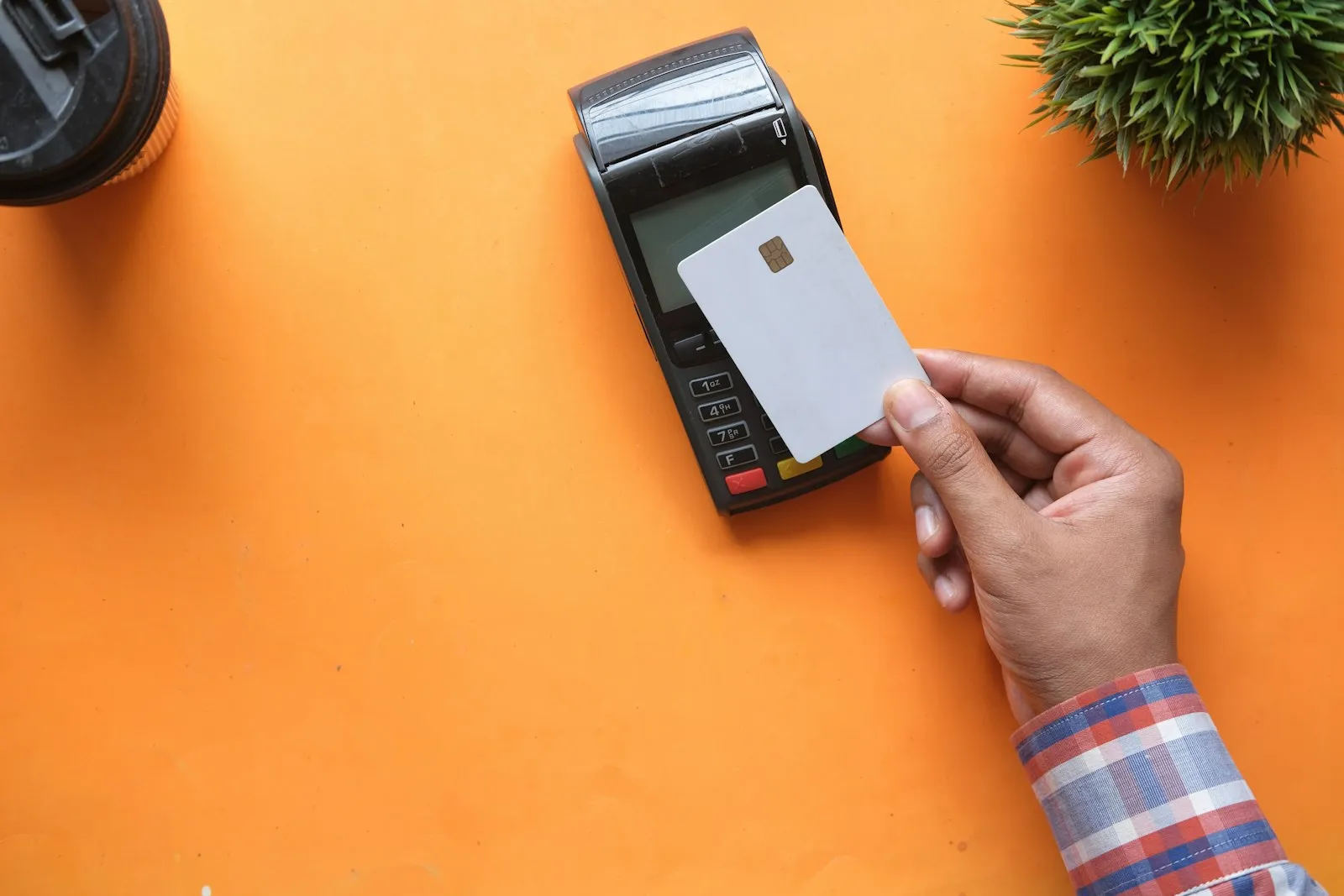A person holds a payment card near a card terminal against an orange background