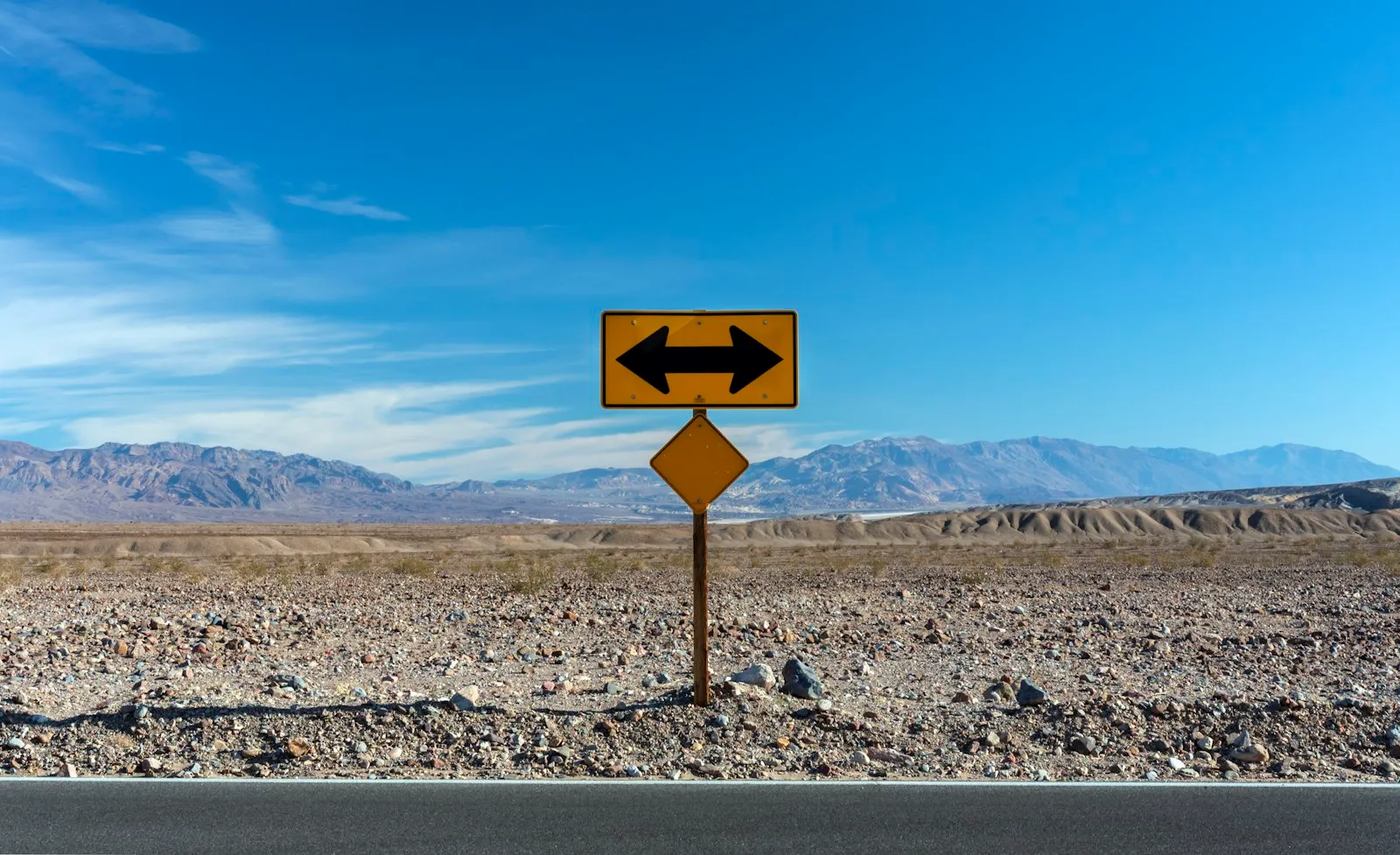 A road sign with two arrows pointing in opposite directions on a desert road