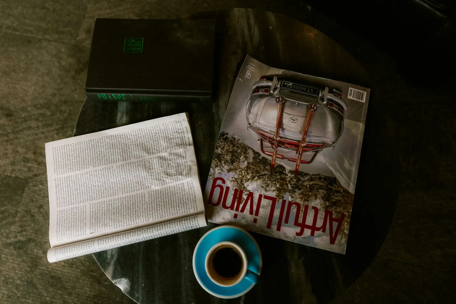 A laptop, a magazine and a newspaper beside a cup of coffee on a table